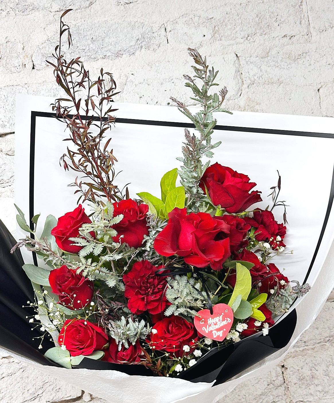 Romantic red Valentine’s Day bouquet wrapped in black and white luxe paper with heart decoration