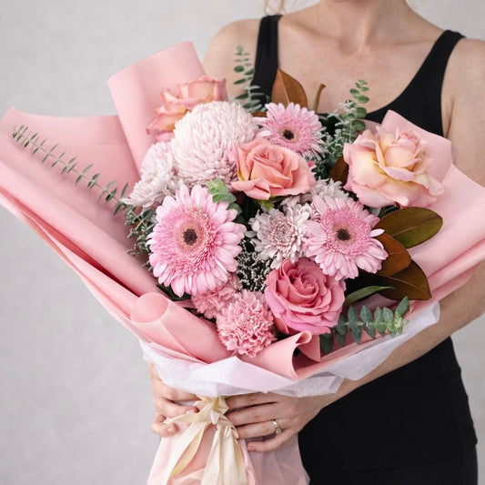 Person holding a bouquet of pink flowers with pink wrapping paper against a gray background