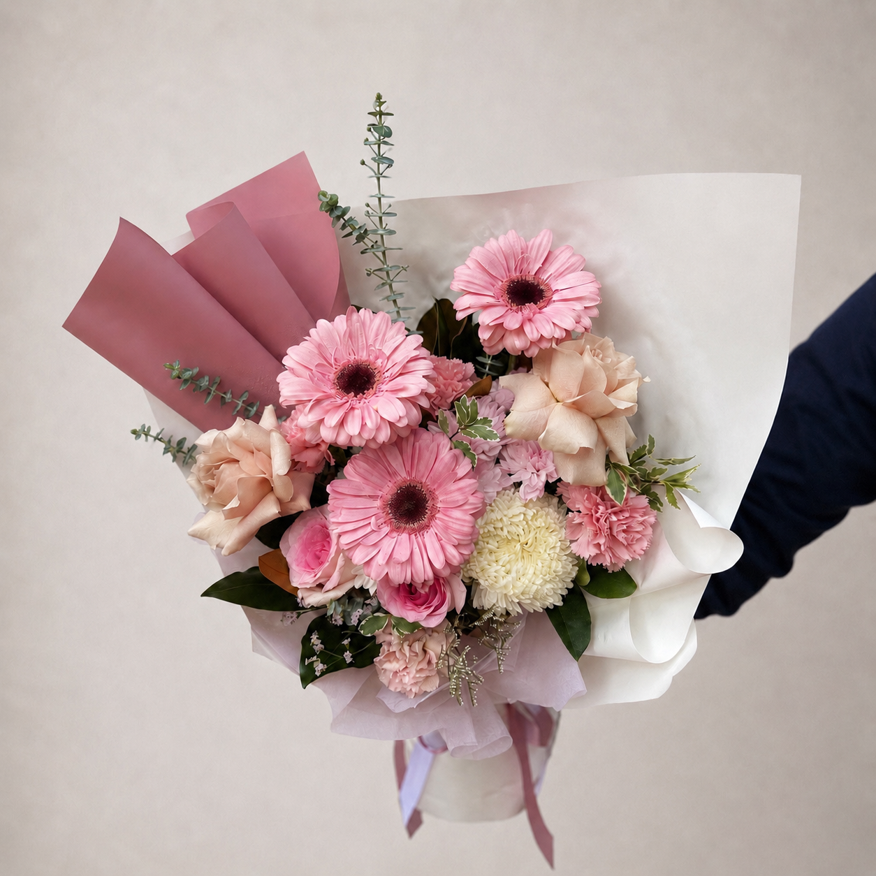 A floral bouquet with pink and peach flowers, green foliage, and pink and white wrapping paper available for same day delivery 