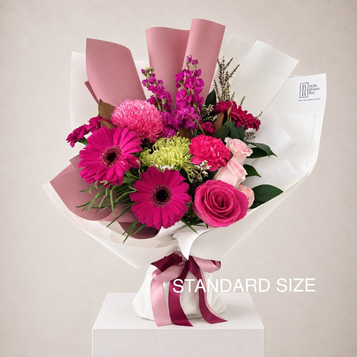 A vibrant floral bouquet wrapped in white and dusty pink paper, featuring bright pink gerberas, pink roses, pink carnations, and green seasonal blooms - same day flower delivery Sydney wide