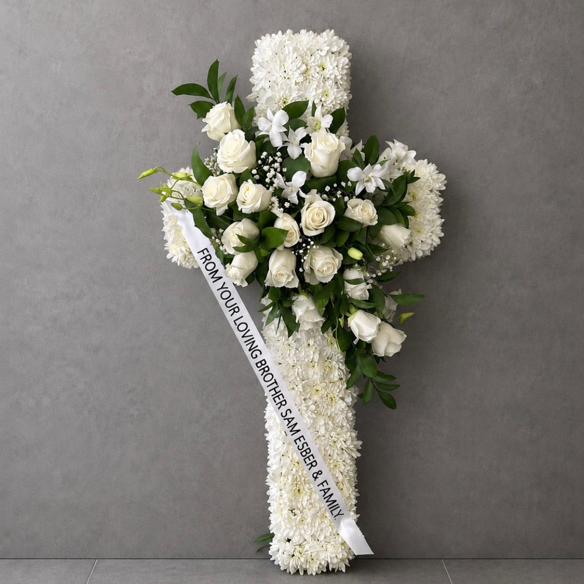 Classic white floral tribute cross with white roses, chrysanthemums and green foliage with a personalised white ribbon.